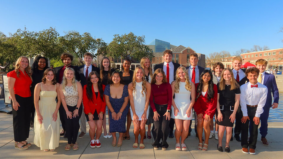 FCLA Class of 2025. Group of young adults in formal attire posing outdoors on a sunny day, surrounded by trees and buildings.